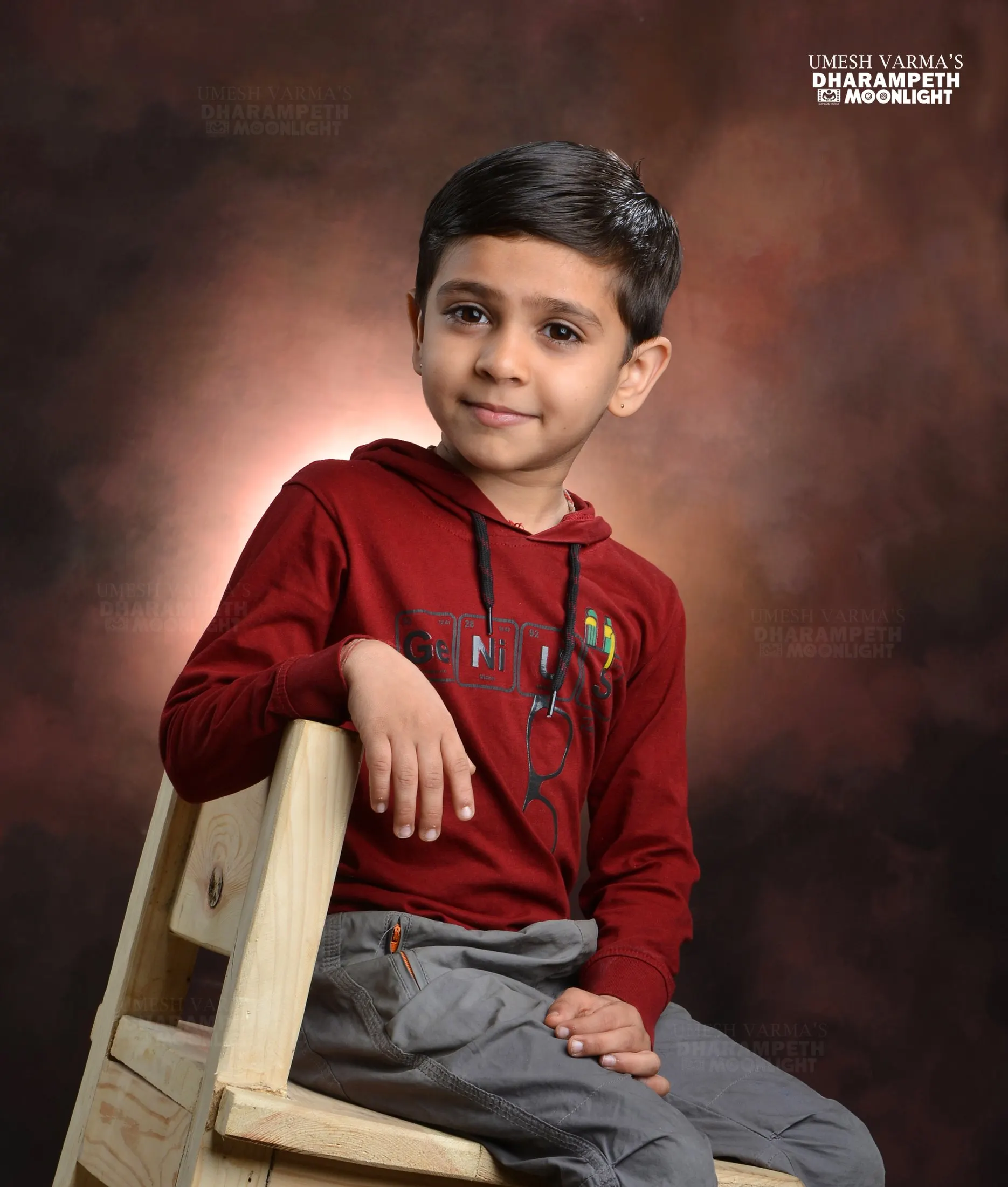 Young boy in a red hoodie sitting on a wooden chair