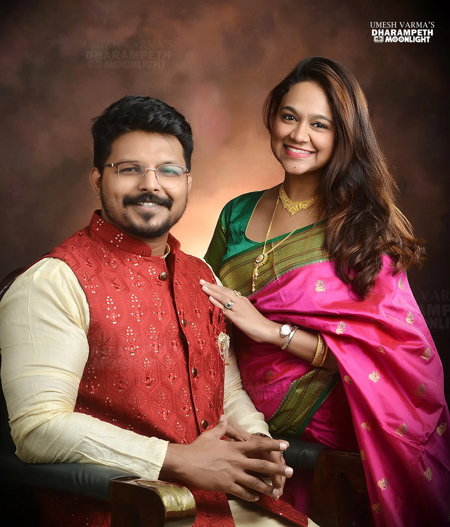 Couple in festive attire, the husband seated and the wife beside him