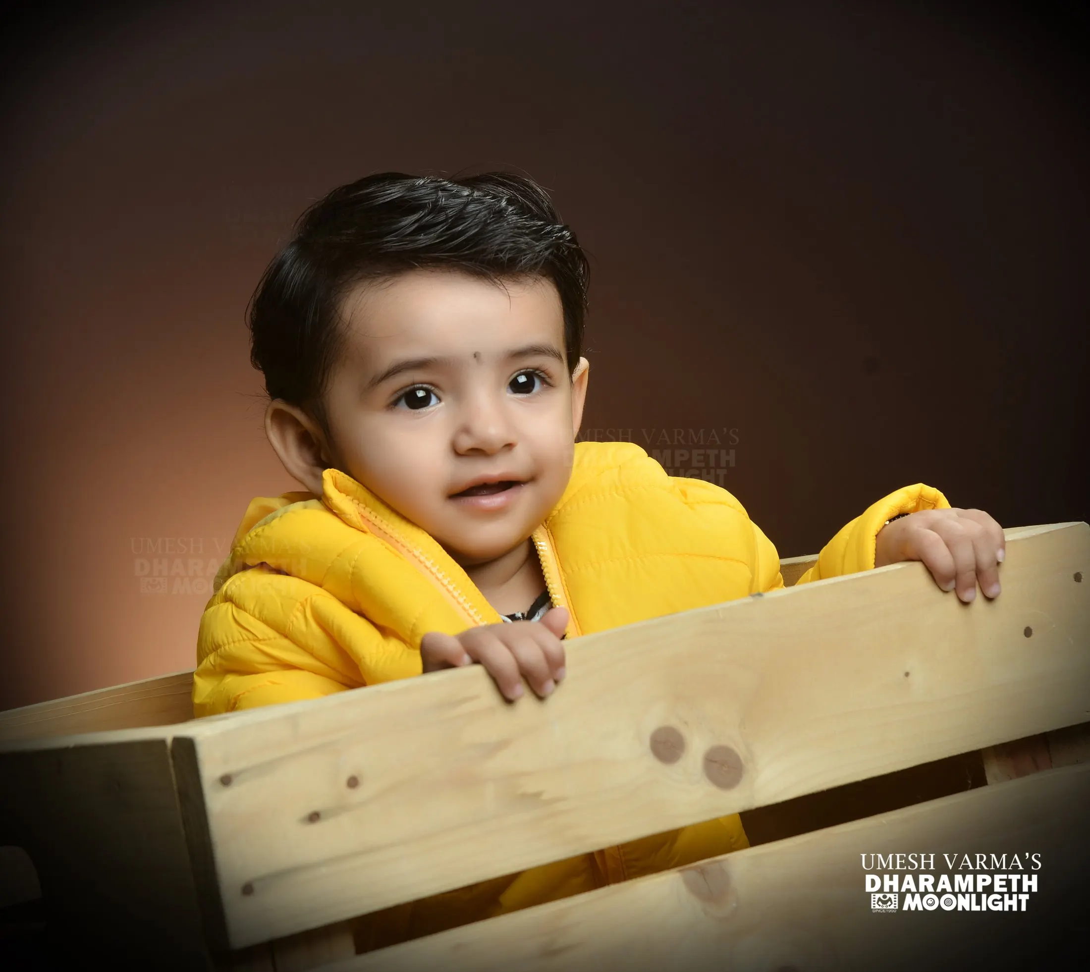 Toddler in a yellow jacket peeking over a wooden crate